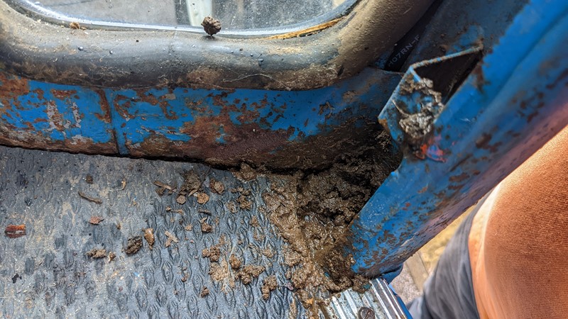 Dirt hiding behind the trim of the Ford 7610 is blocking drain holes.